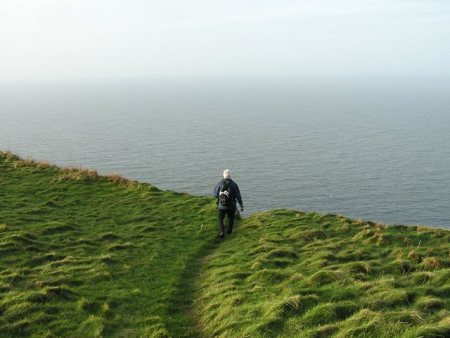 View of walker looking out from clifftop across hazy sea